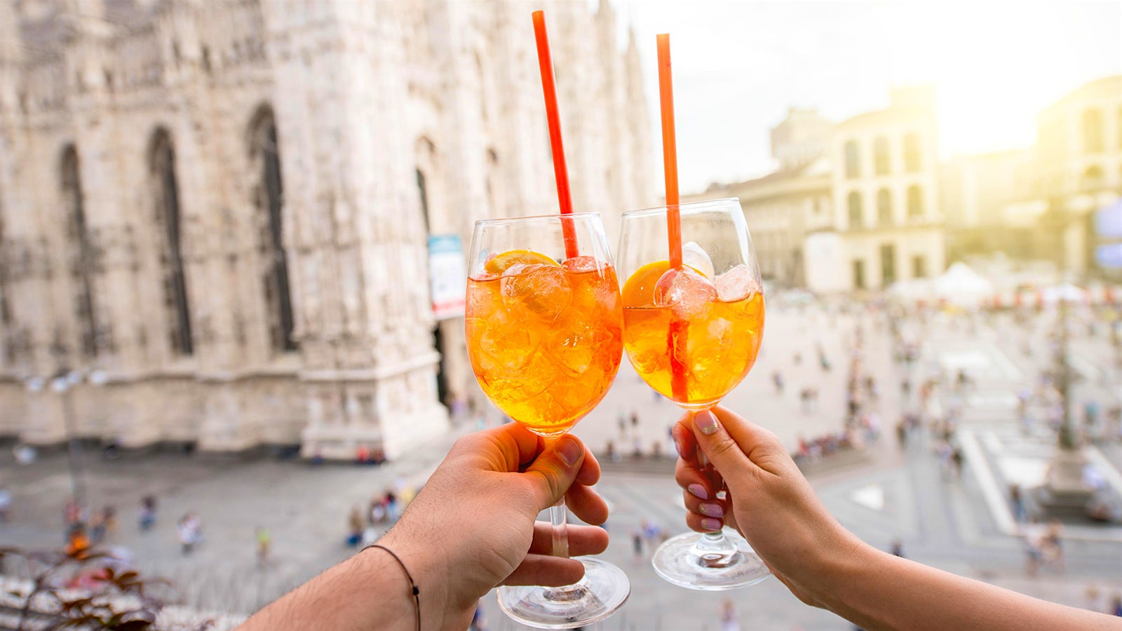  Two people sheers with glasses of Aperol spritz.